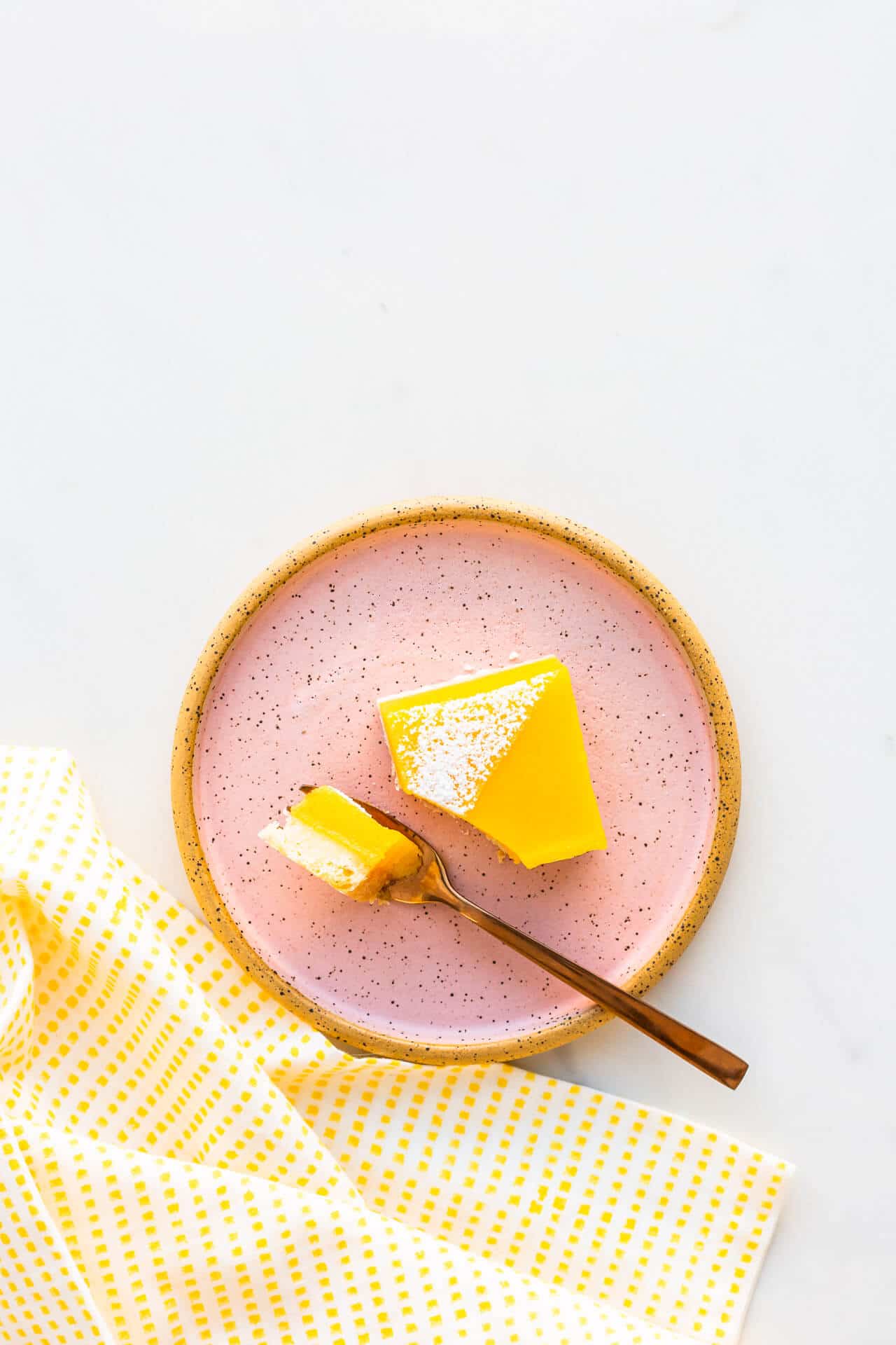 A pink ceramic plate with a lemon bar and a fork.