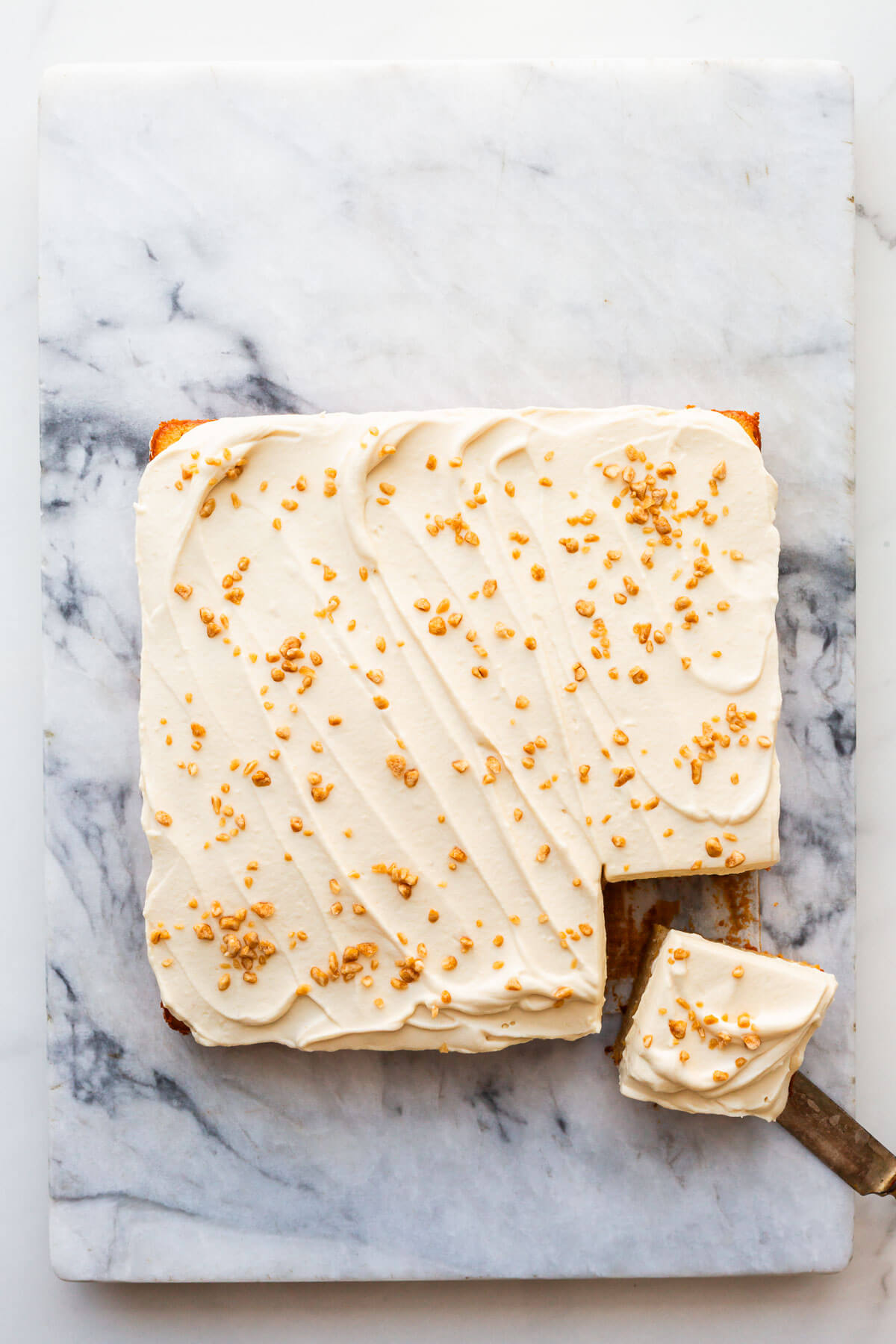 A square maple cake being cut into squares on a marble slab.