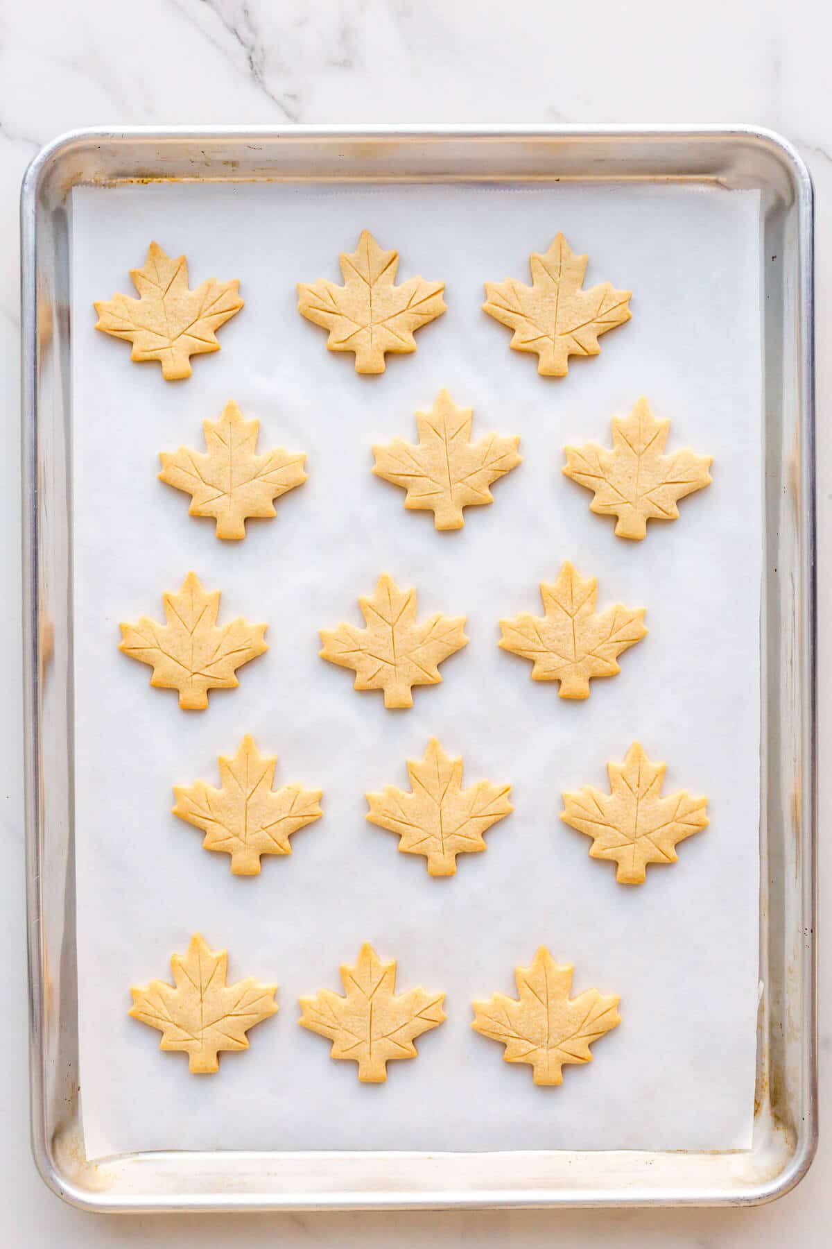 Freshly baked maple leaf-shaped cookies on a sheet pan