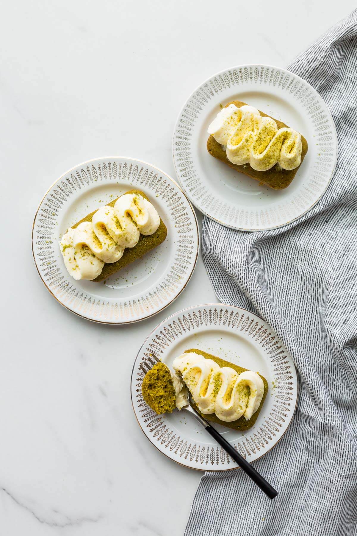 Mini matcha cakes with white chocolate frosting piped on top, served on dessert plates.