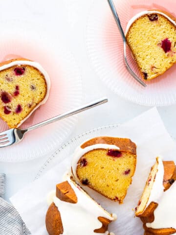 Slices of orange cranberry cake served on pink glass plates with forks.
