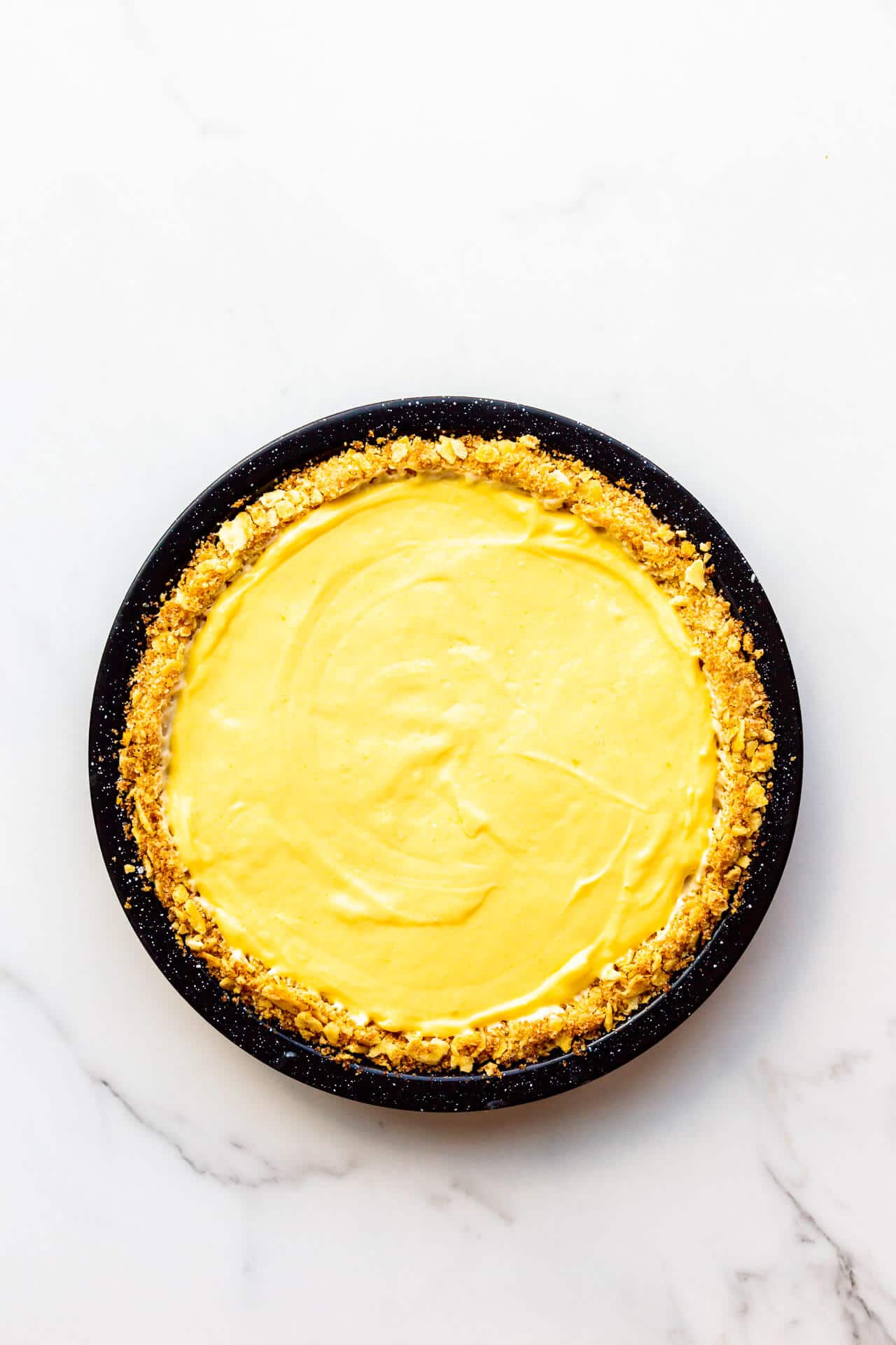 Orange curd filled pie with saltine crust in black speckled pie plate.