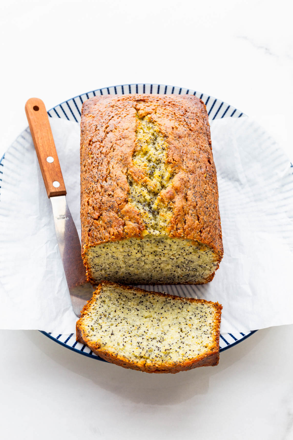 Slicing a glazed orange cake with poppy seeds.