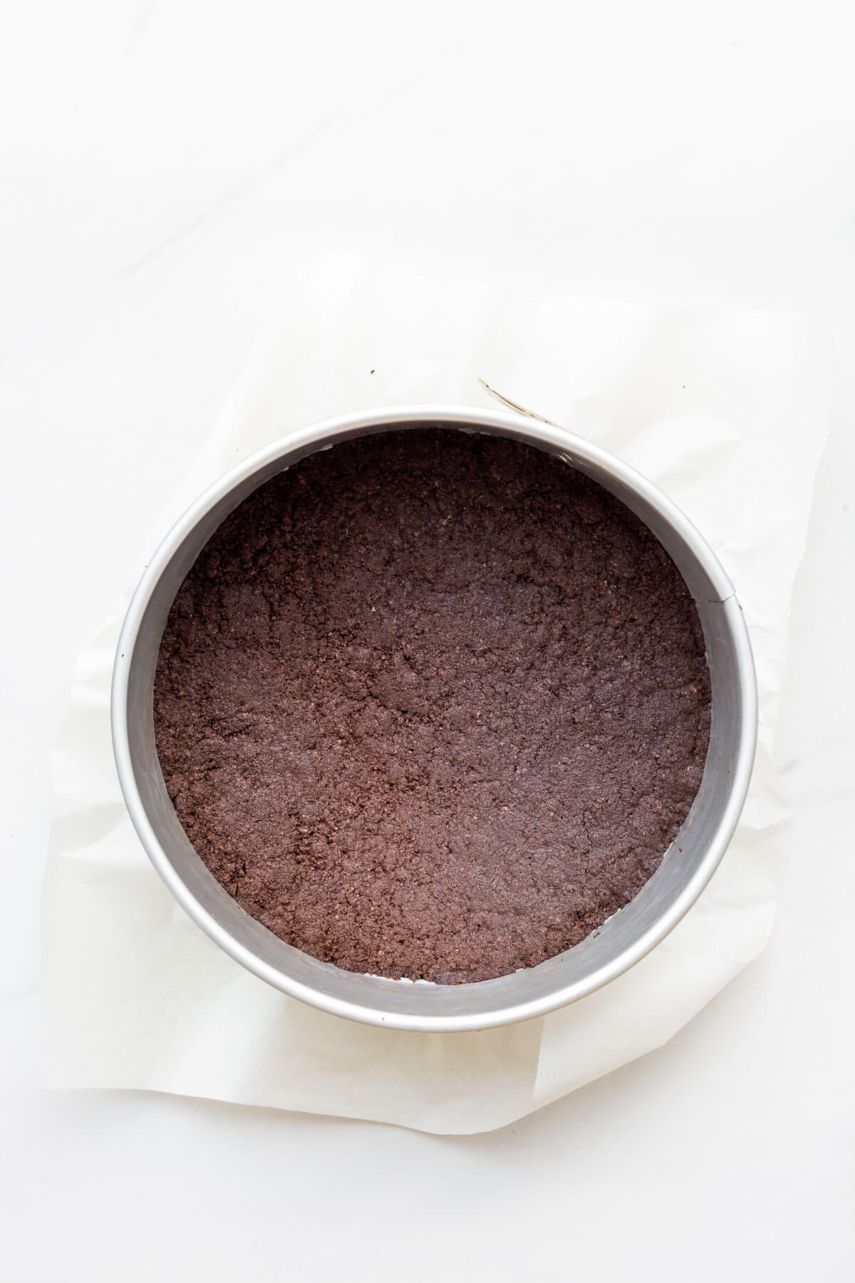 Oreo cookie crust baked in a springform pan lined with parchment paper for a cheesecake recipe.