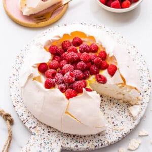 Pavlova cake filled with whipped cream, lemon curd, and raspberries being served.