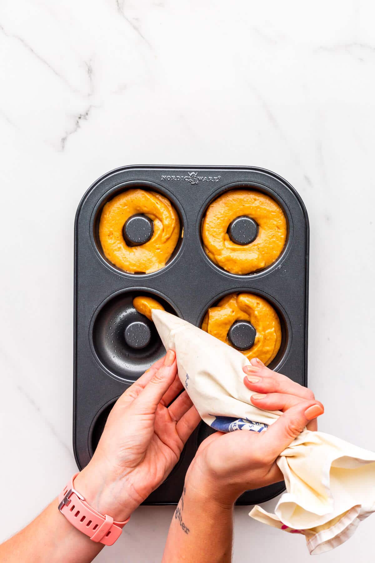 Piping pumpkin donut batter into a donut pan to make baked donuts.