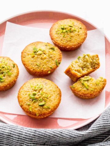 A pink plate with pistachio financiers, one of them broken open to show the crumb.