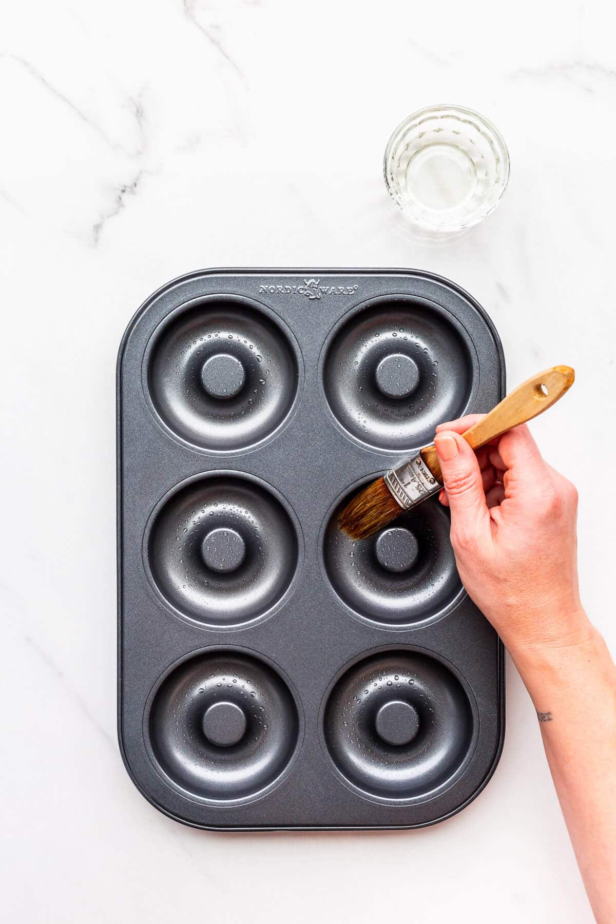 Preparing a non-stick donut pan to bake donuts by brushing the cavities with canola oil to make sure the donuts don't stick.