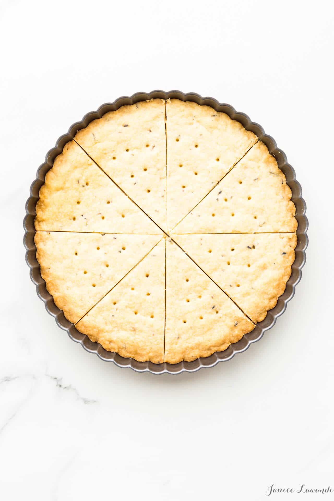 Press shortbread cookie dough into a tart pan with a crinkled edge, score, bake, and cut again for perfect triangle shortbread wedges