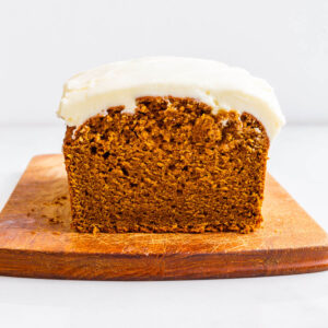 Whole wheat pumpkin loaf cake topped with a thick layer of cream cheese frosting on a cutting board.