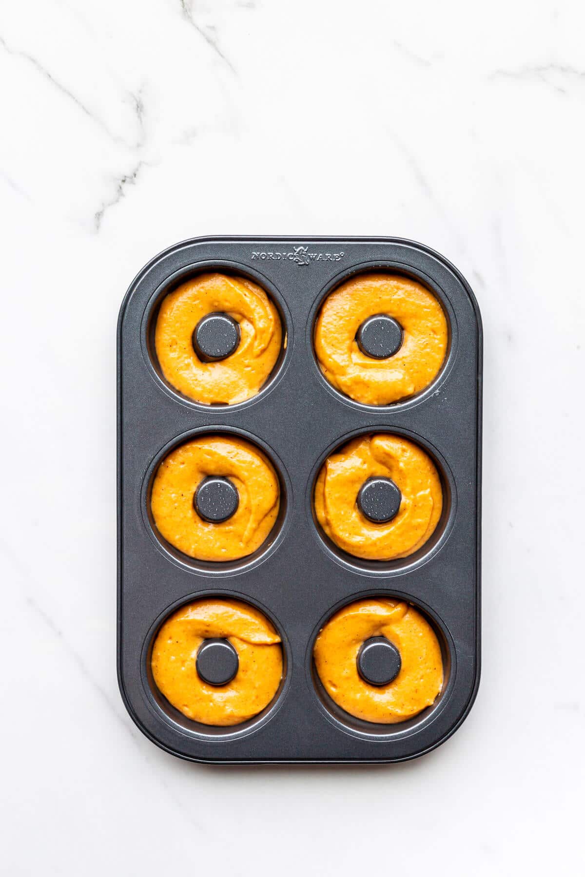 Pumpkin donuts in a donut pan before baking.
