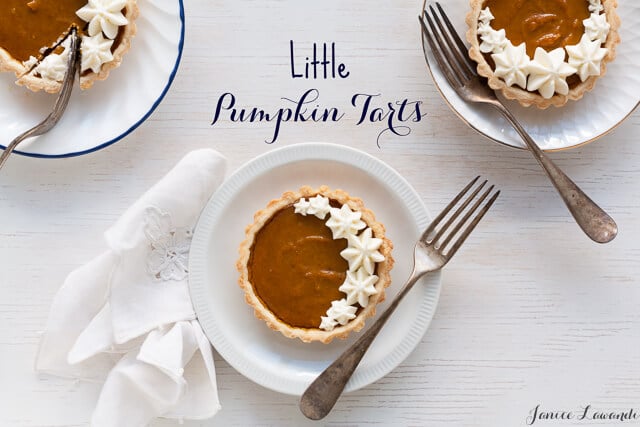 Individual pumpkin tarts garnished with sweetened whipped cream piped on top, served on white plates.