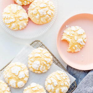 Lemon crinkle cookies on a cooling rack with some transferred to pink plates.