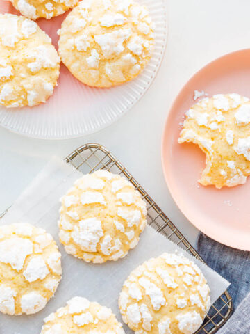 Lemon crinkle cookies on a cooling rack with some transferred to pink plates.