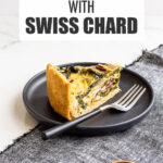 A slice of quiche with rainbow Swiss chard in it on a black plate with a fork, served with a small bowl of salt on the side.