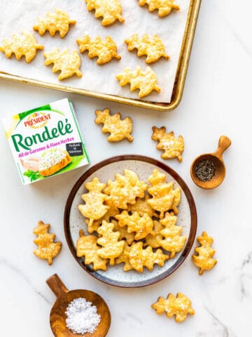 Baked savoury cheese shortbread biscuits shaped like oak leaves being transferred from a sheet pan to a ceramic plate