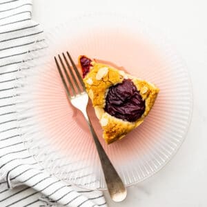 A slice of plum cake on a pink glass plate.