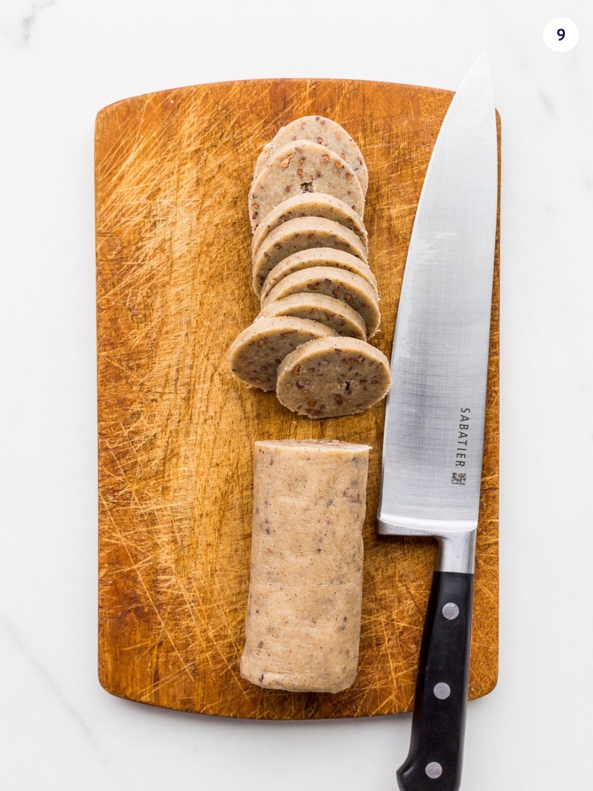 Slicing a log of shortbread cookie dough on a cutting board with a chef's knife.