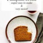 A slice of pumpkin bread on a ceramic plate with a green linen and a cup of tea