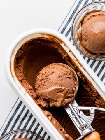 Scooping chocolate ice cream with an ice cream scoop into glass bowls.