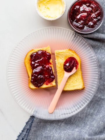 Toast served with homemade strawberry jam and butter on a pink plate.