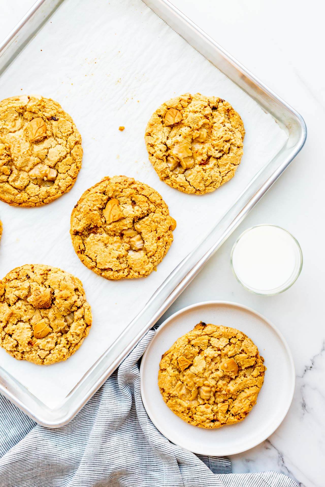 Serving maple cookies from a sheet pan onto a plate with a glass of milk on the side.