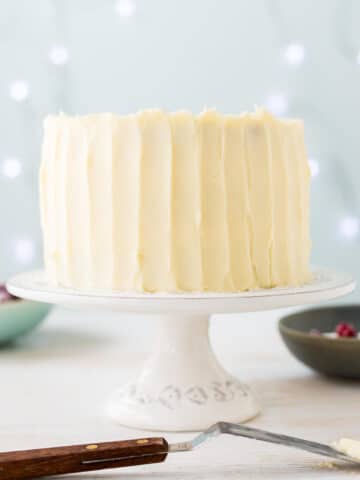 Thick cream cheese frosting on a layer cake, spread with an offset spatula to create vertical streaks on the surface of the frosting.