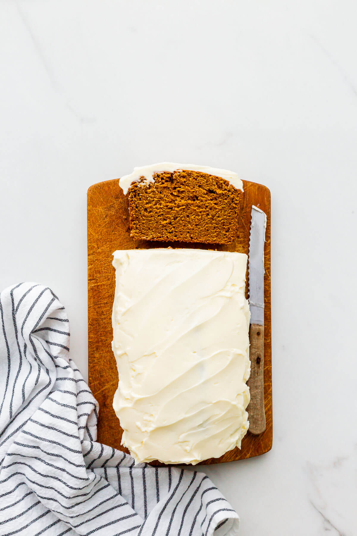 Slicing a whole wheat pumpkin bread with cream cheese frosting on a wood cutting board.