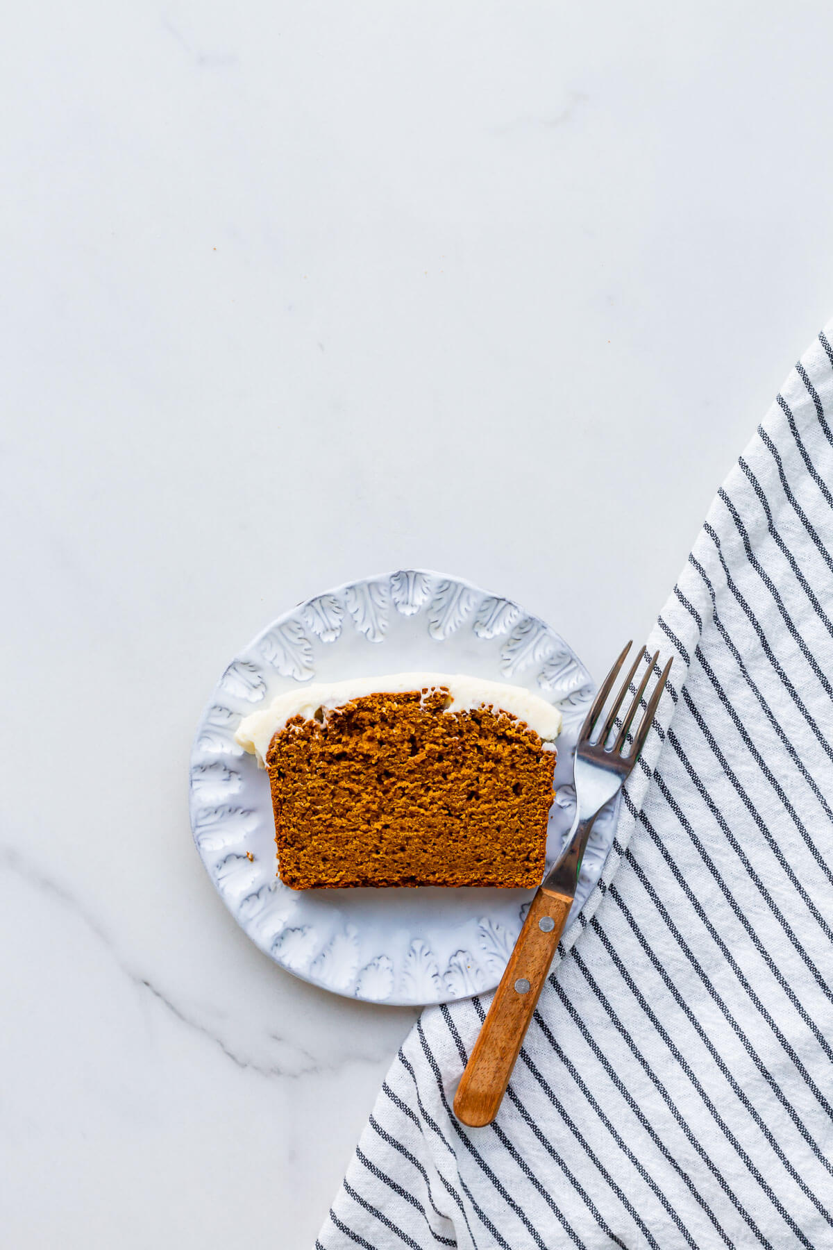 A slice of pumpkin bread with cream cheese frosting on a dessert plate.