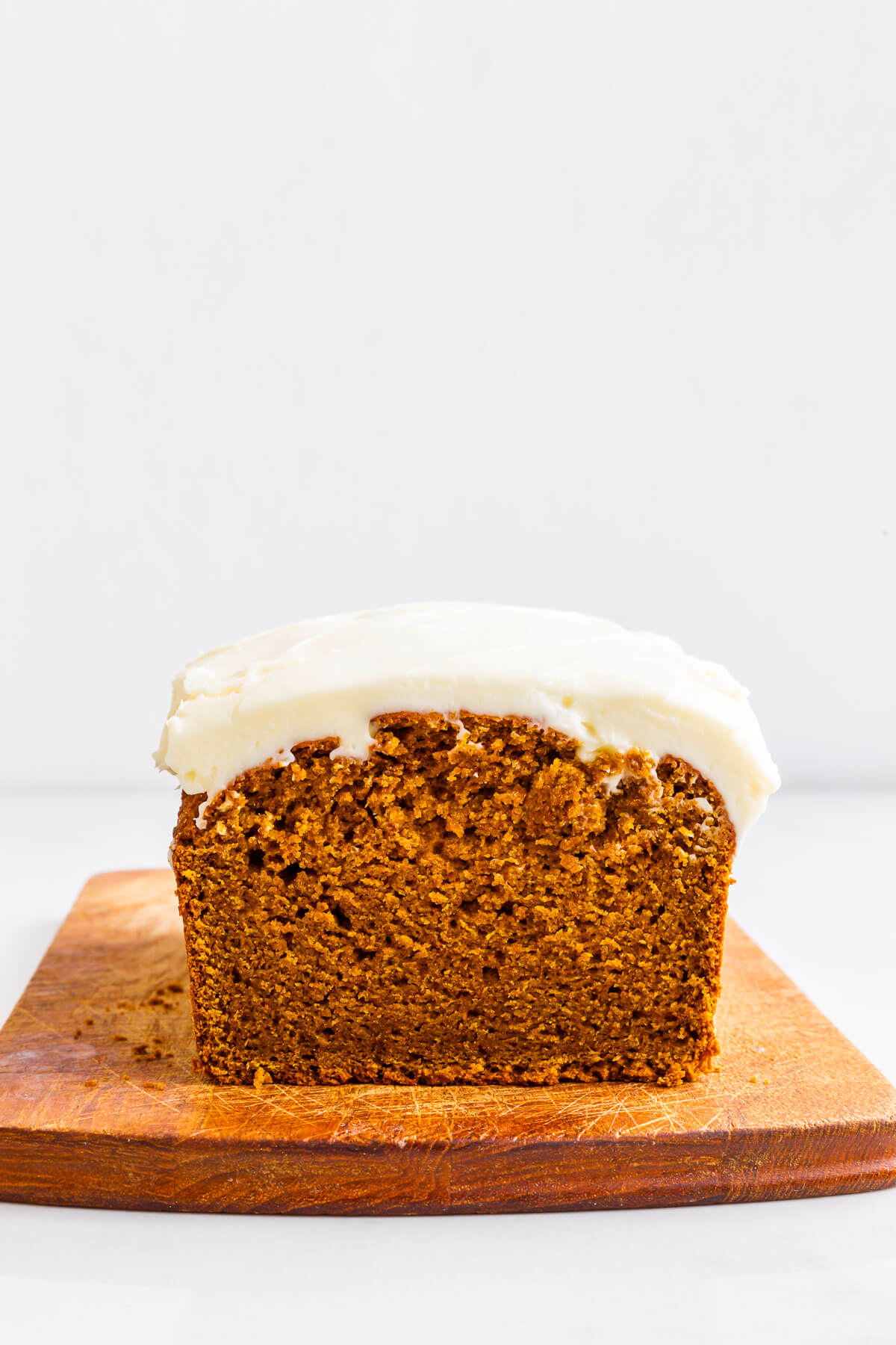 Whole wheat pumpkin bread topped with a thick layer of cream cheese frosting on a wood cutting board.